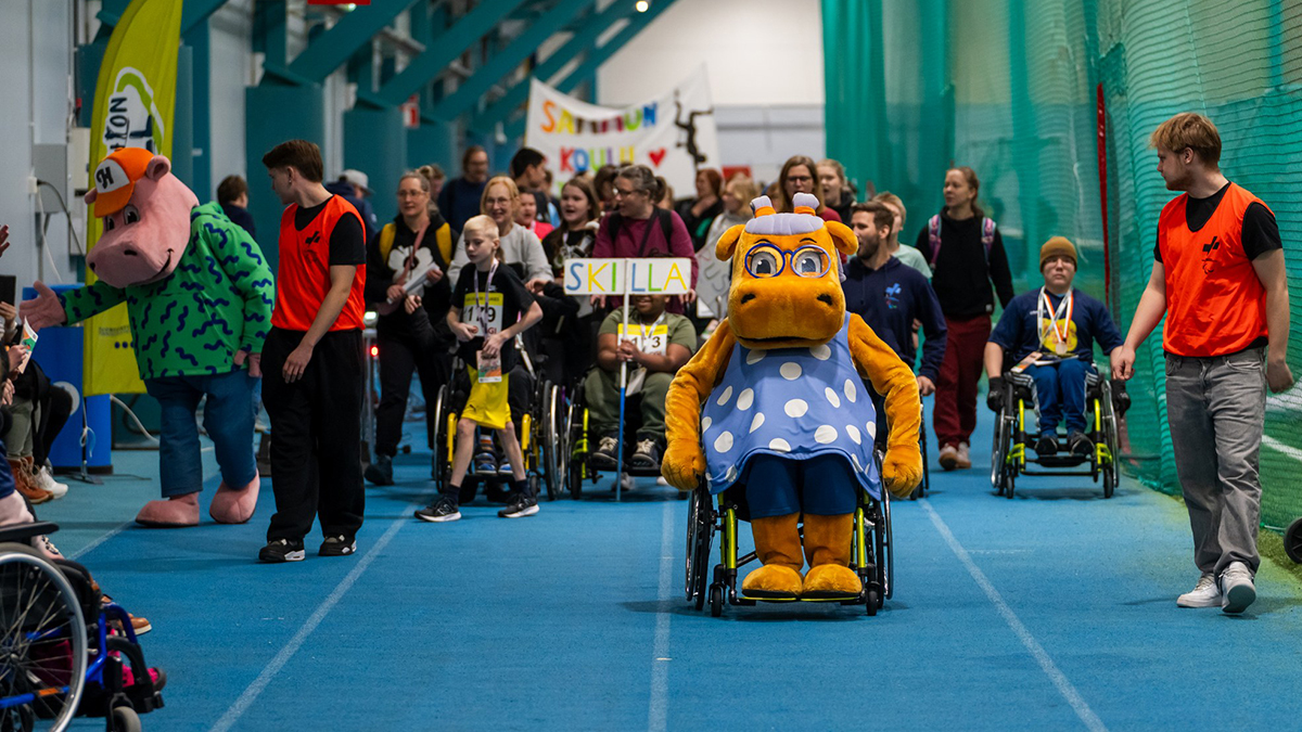 Avajaiskulkue lähestyy kameraa Pajulahtihallin sinistä juoksurataa pitkin. Etunenässä kulkee OP:n Hippo-hahmo pyörätuolia käyttäen.